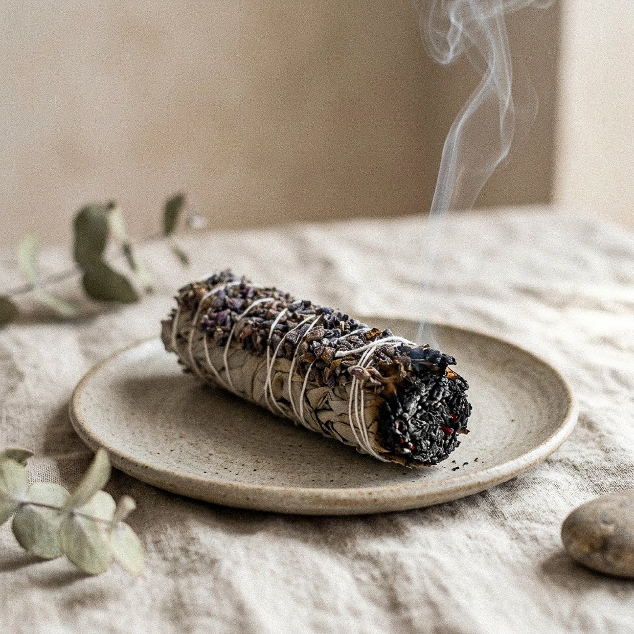 Bâton de sauge blanche et lavande allumé dégageant une fine fumée sur une coupelle en céramique beige - Myvelyshop