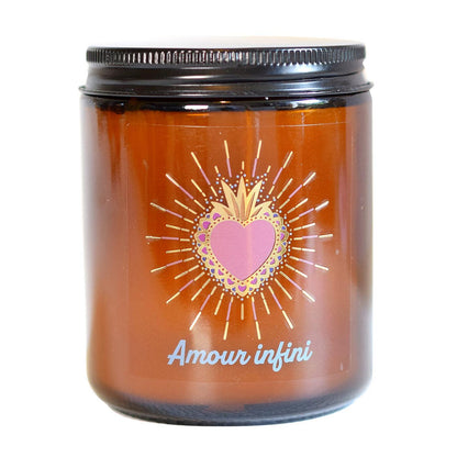 Bougie parfumée en pot de verre ambré fermé par un couvercle noir, ornée d'une étiquette avec un cœur sacré radiant et l'inscription "Amour infini".