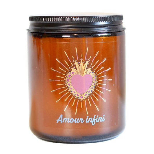 Bougie parfumée en pot de verre ambré fermé par un couvercle noir, ornée d'une étiquette avec un cœur sacré radiant et l'inscription "Amour infini".
