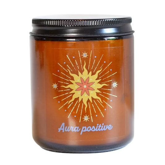 Pot de bougie en verre ambré fermé par son couvercle noir, orné d'une étiquette représentant un soleil rayonnant et l'inscription "Aura positive".