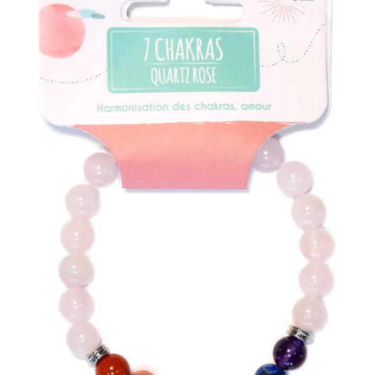Gros plan sur un bracelet de perles en quartz rose avec des perles de chakra colorées et des intercalaires en métal, présenté sur un emballage cartonné portant l'inscription "7 CHAKRAS QUARTZ ROSE" et "Harmonisation des chakras, amour".