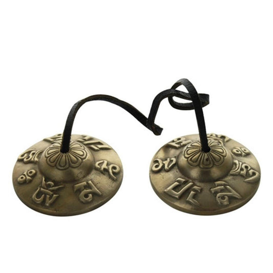 Paire de cymbales tibétaines en bronze gravées de symboles sacrés bouddhistes et reliées par un lien en cuir noir, présentées à plat sur fond blanc.