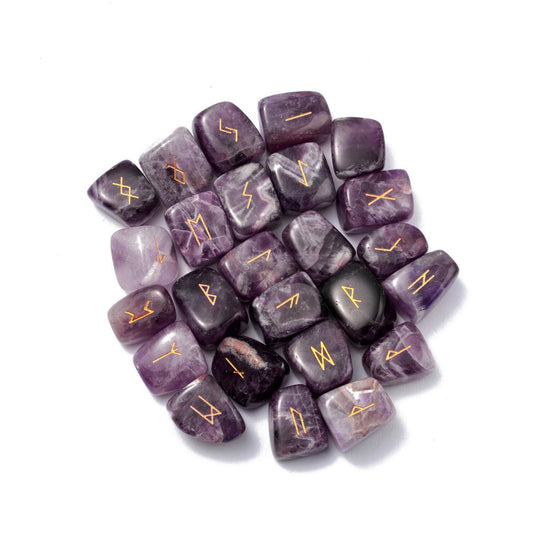 Ensemble de 25 runes divinatoires en améthyste naturelle polie aux nuances violettes avec gravures dorées des symboles Futhark, regroupées au centre sur un fond blanc pur.